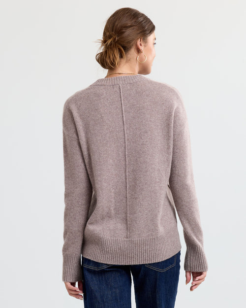 Woman wearing a latte-colored cashmere sweater with ribbed cuffs and hem, viewed from the back against a white background
