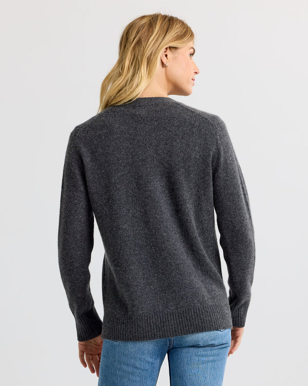 LIFESTYLE / EDITORIAL: Woman wearing charcoal cashmere sweater and blue jeans, viewed from the back against a plain