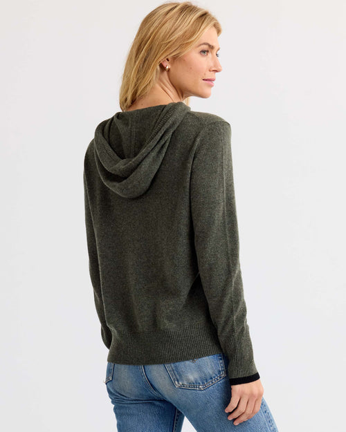 Woman wearing dark olive cashmere hoodie and blue jeans, shown from back and side, standing against white background