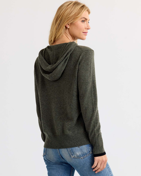 Woman wearing dark olive cashmere hoodie and blue jeans, shown from back and side, standing against white background