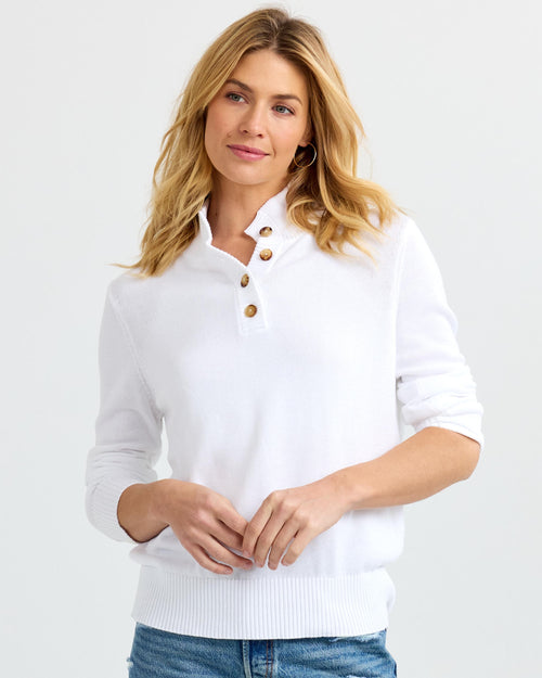 Front view image of a woman wearing a white buttoned cashmere sweater with sleeves pushed up and blue jeans