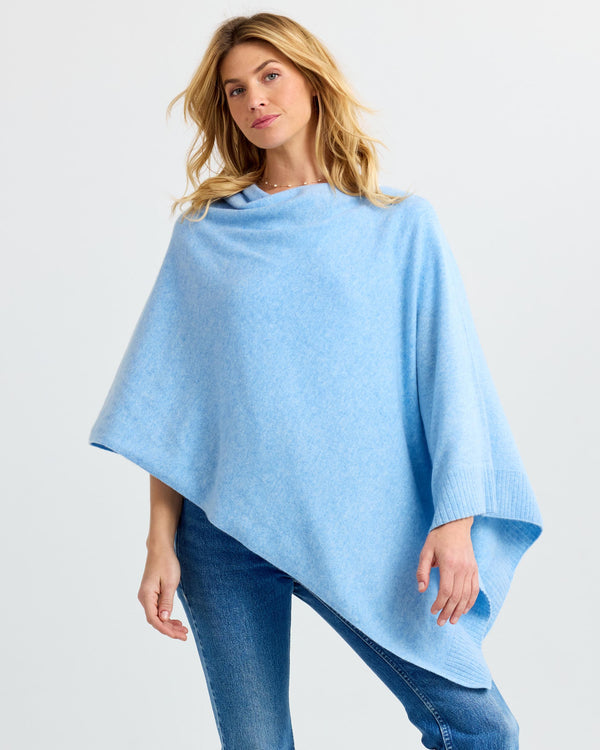 LIFESTYLE / EDITORIAL: Woman wearing light blue asymmetrical cashmere poncho with jeans against white background