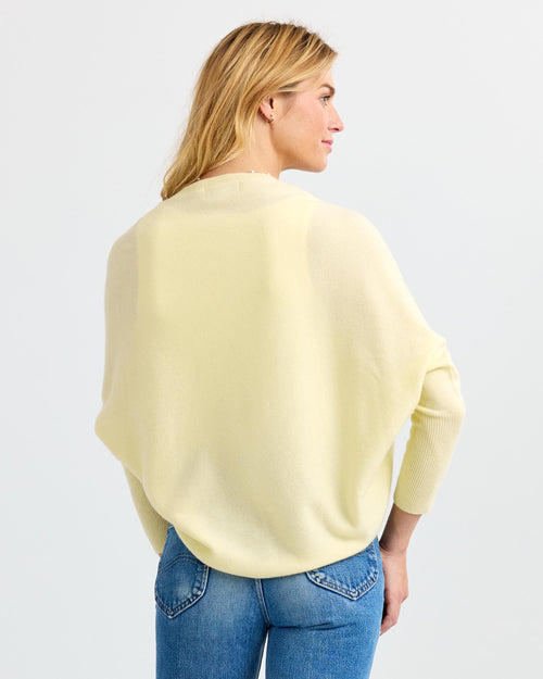 Woman wearing buttermilk yellow cashmere sweater and blue jeans, shown from the back against a white background