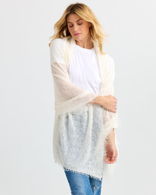 LIFESTYLE / EDITORIAL: Woman wearing a white cashmere shawl over a white shirt and blue jeans against a plain background