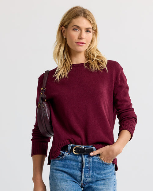LIFESTYLE / EDITORIAL: Woman wearing merlot-colored cashmere sweater and jeans with a matching shoulder bag against white