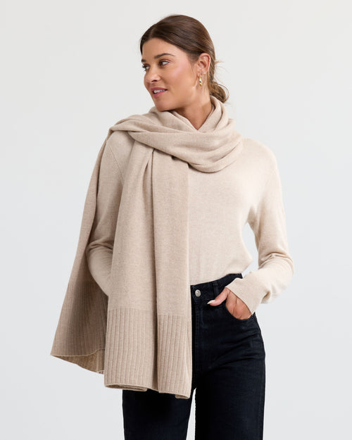 Woman wearing cappuccino cashmere sweater and matching scarf with black pants against plain background