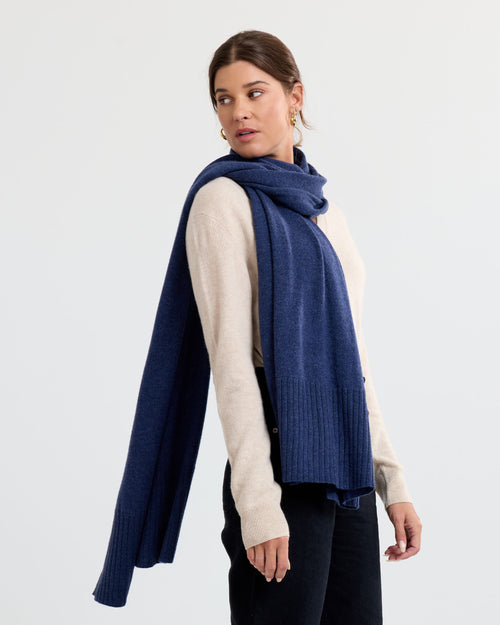 Side view image of a woman wearing an indigo cashmere scarf draped over a beige sweater against a plain background