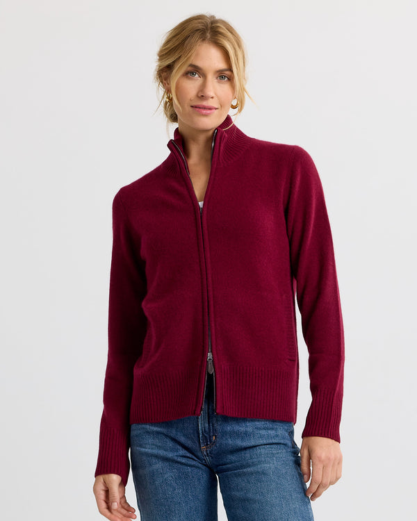 LIFESTYLE / EDITORIAL: Woman wearing a barolo red zip-up cashmere sweater and blue jeans against a plain background