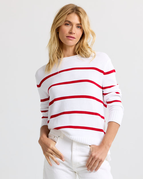 LIFESTYLE / EDITORIAL: Woman wearing white sweater with red horizontal stripes and white pants against plain background
