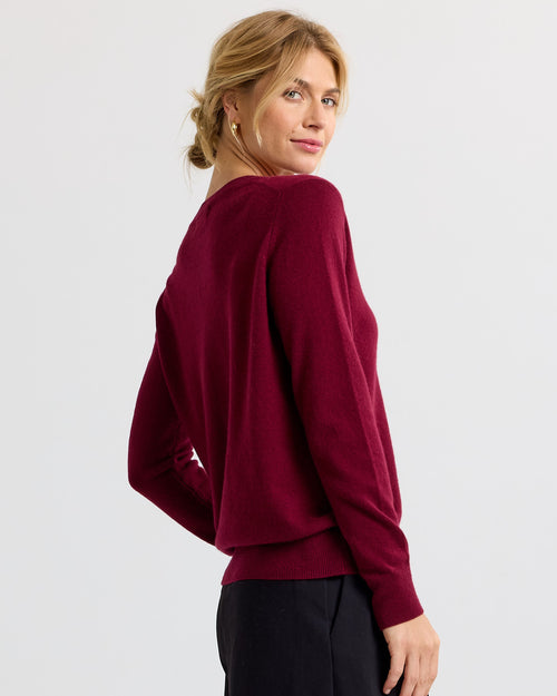 LIFESTYLE / EDITORIAL: Woman wearing a barolo-colored cashmere sweater, looking over her shoulder against a plain background