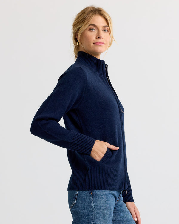 LIFESTYLE / EDITORIAL: Woman in navy zip-up cashmere sweater with hands in pockets, side view, plain background