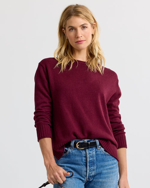 Woman wearing merlot-colored cashmere sweater and blue jeans against plain background