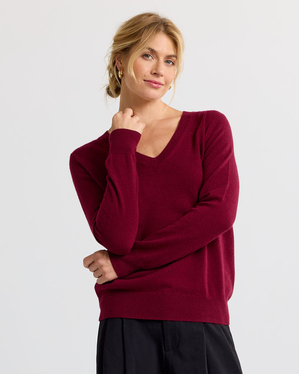 LIFESTYLE / EDITORIAL: Woman wearing a barolo red V-neck cashmere sweater with black pants, standing against a white