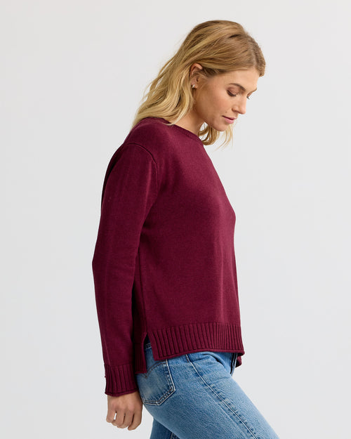 LIFESTYLE / EDITORIAL: Woman in merlot-colored cashmere sweater and blue jeans, side view against plain background