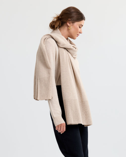 LIFESTYLE / EDITORIAL: Woman wearing beige cashmere sweater and scarf, standing in profile against plain background