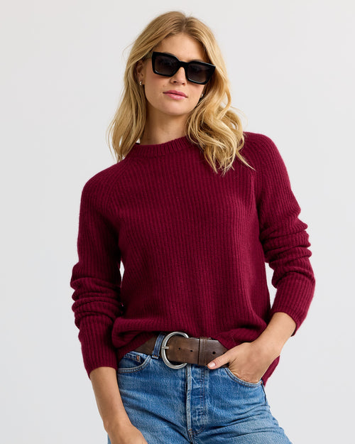 Front view image of a woman wearing a barolo red ribbed cashmere sweater with blue jeans and black sunglasses
