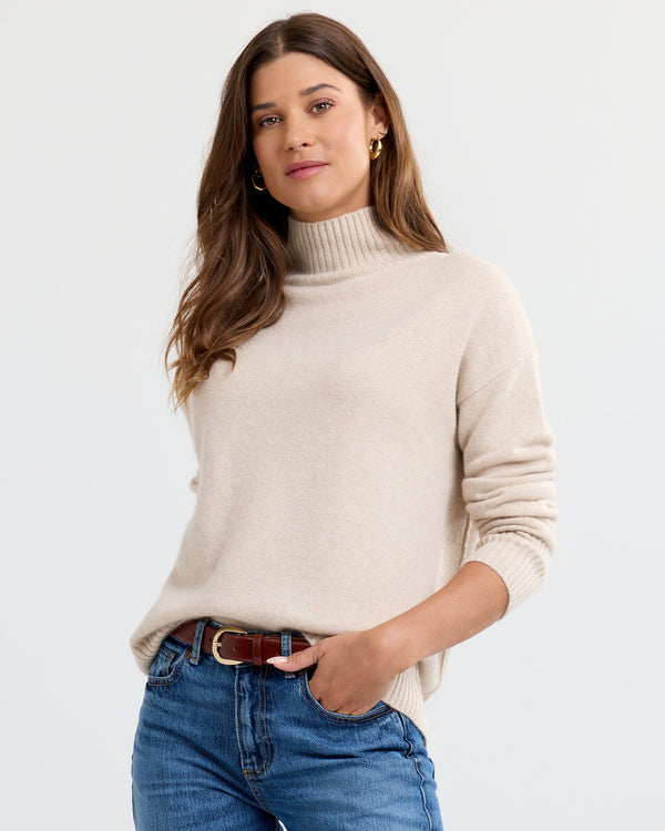Oatmeal cashmere funnel neck sweater with blue jeans, three-quarter view with hand in pocket