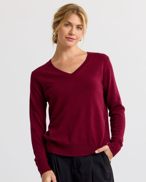 Woman wearing a barolo-colored V-neck cashmere sweater with long sleeves and black pants, standing against a white background