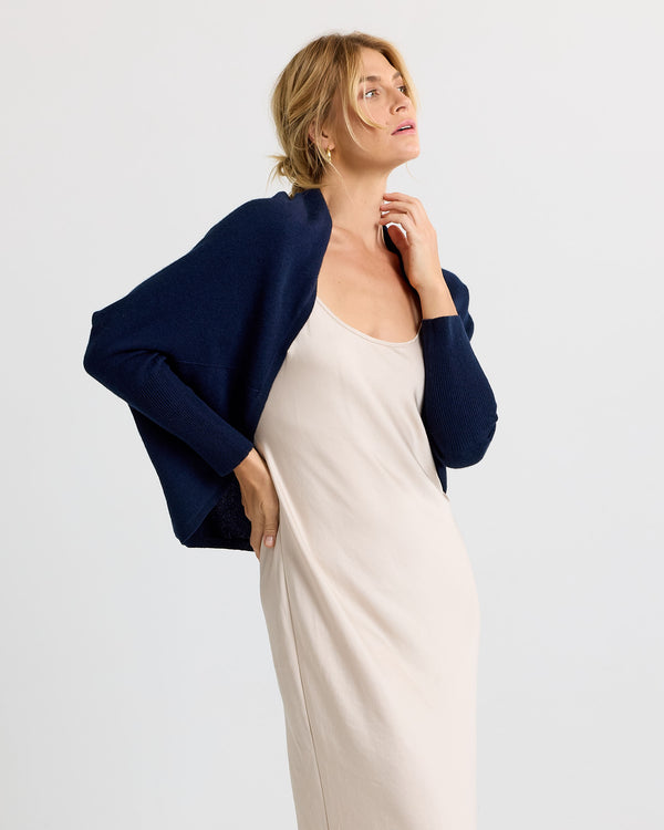 Side view image of a woman wearing a navy cashmere cardigan over a beige slip dress against a plain background