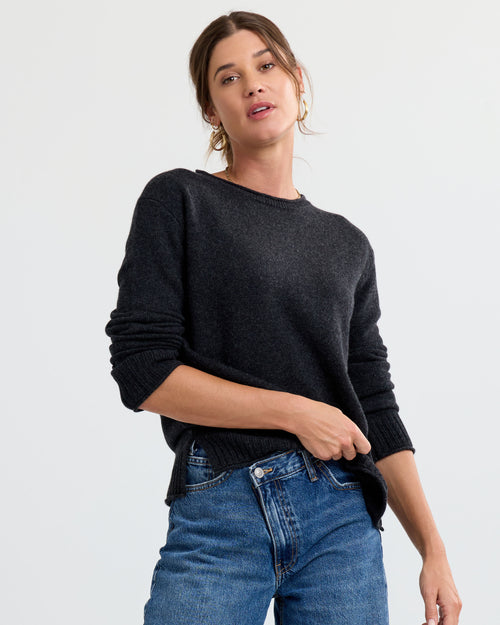 LIFESTYLE / EDITORIAL: Woman wearing charcoal cashmere sweater and blue jeans against plain background