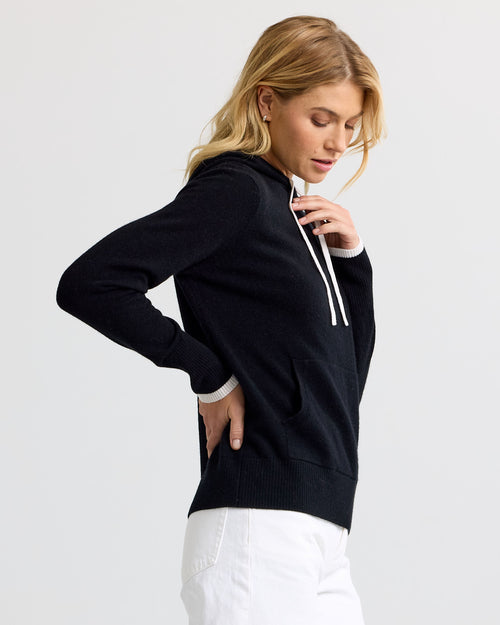 LIFESTYLE / EDITORIAL: Woman wearing black cashmere hoodie with white drawstrings and white pants, side profile view