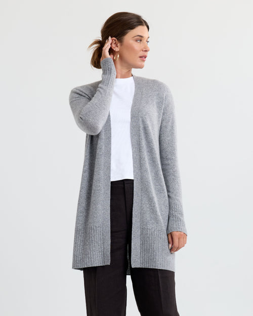 Three-quarter view image of a woman wearing a long grey cashmere cardigan with a white top and black pants