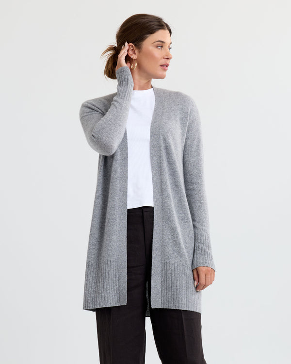 Three-quarter view image of a woman wearing a long grey cashmere cardigan with a white top and black pants