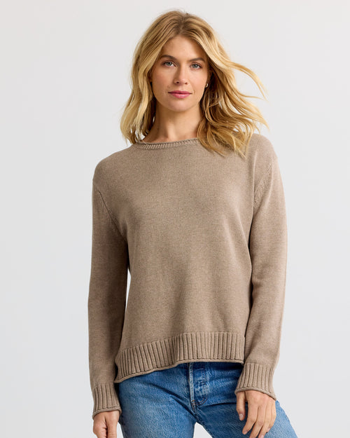 Front view image of a woman wearing a taupe cashmere sweater and blue jeans standing against a plain background