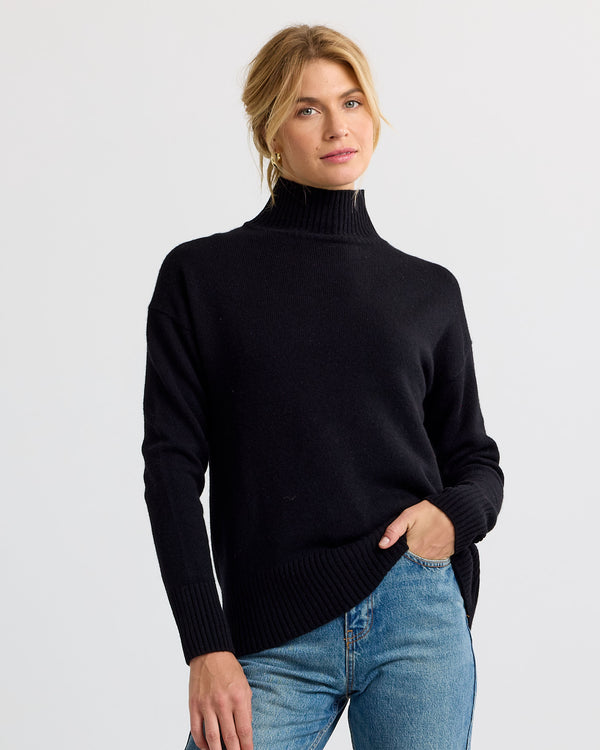 Black cashmere funnel neck sweater with blue jeans, standing full-length view