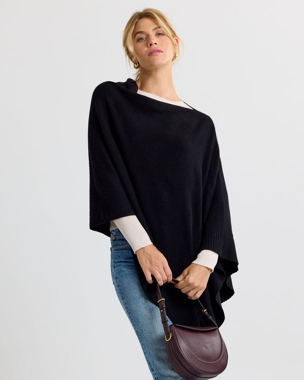 LIFESTYLE / EDITORIAL: Woman wearing black cashmere poncho, white long sleeve top, blue jeans, holding brown leather handbag