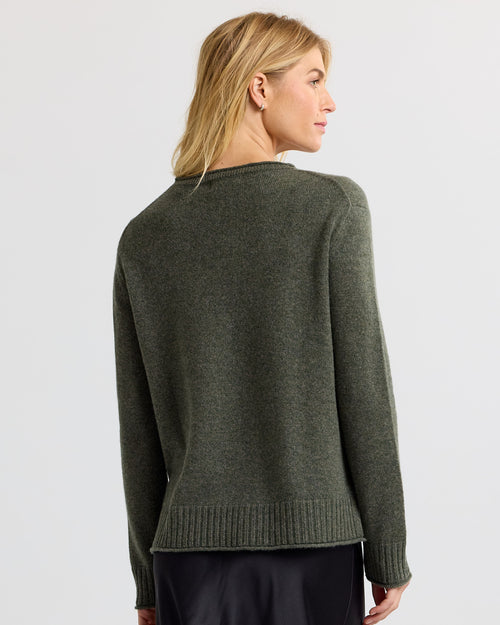 Woman wearing dark olive cashmere sweater, shown from back, standing against plain light gray background