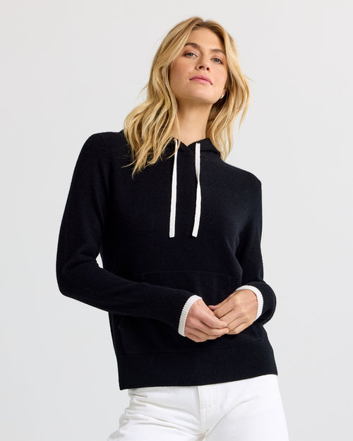 LIFESTYLE / EDITORIAL: Woman wearing black cashmere hoodie with white drawstrings and cuffs, paired with white pants