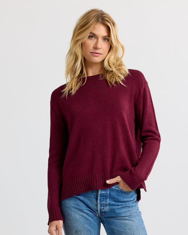 Woman wearing merlot-colored cashmere sweater and blue jeans, standing against a plain light background