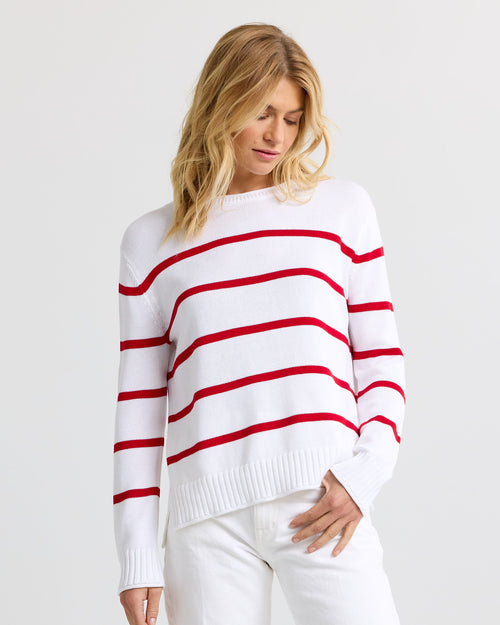 Three-quarter view image of a woman wearing a white cashmere sweater with red stripes and white pants.