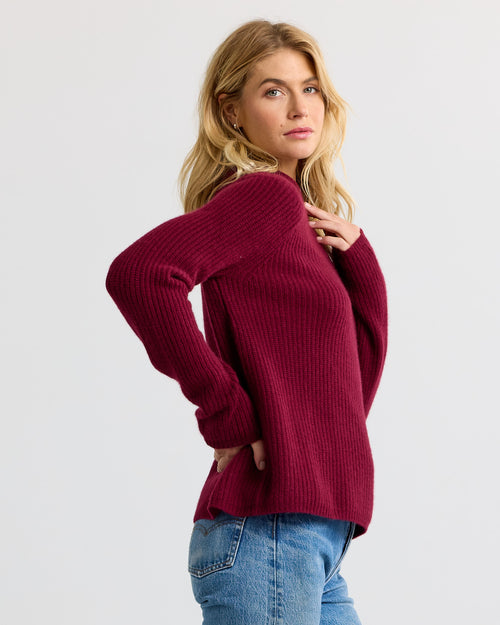 Woman in side profile wearing a barolo-colored ribbed cashmere sweater and blue jeans against a plain background