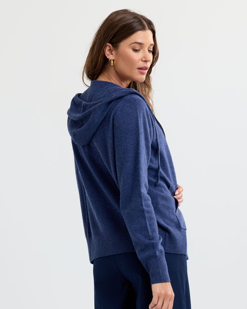 Woman wearing indigo cashmere hoodie, side view, with long sleeves and ribbed cuffs against white background