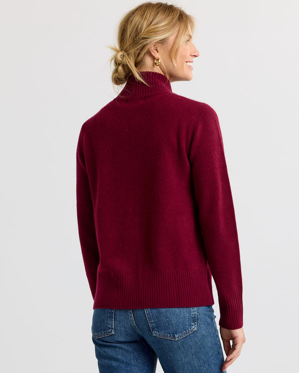 Woman wearing a barolo-colored cashmere turtleneck sweater, shown from the back, paired with blue jeans