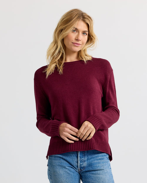 LIFESTYLE / EDITORIAL: Woman wearing merlot-colored cashmere sweater and blue jeans against plain background