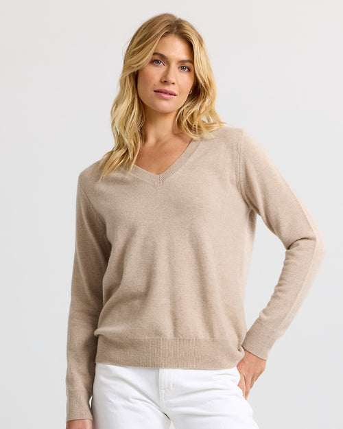 Front view image of a woman wearing a cappuccino V-neck cashmere sweater and white pants with hand on hip