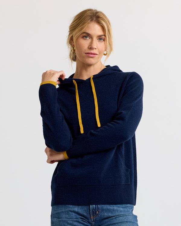 Woman wearing navy blue cashmere hoodie with yellow drawstrings and cuffs, standing against plain white background