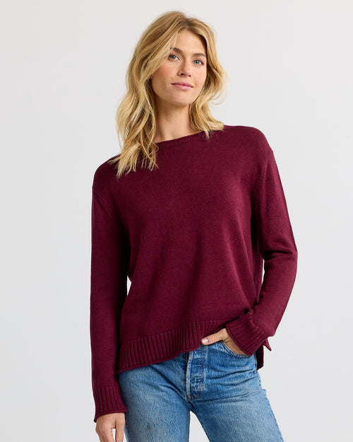LIFESTYLE / EDITORIAL: Woman wearing merlot-colored cashmere sweater and blue jeans against a plain background