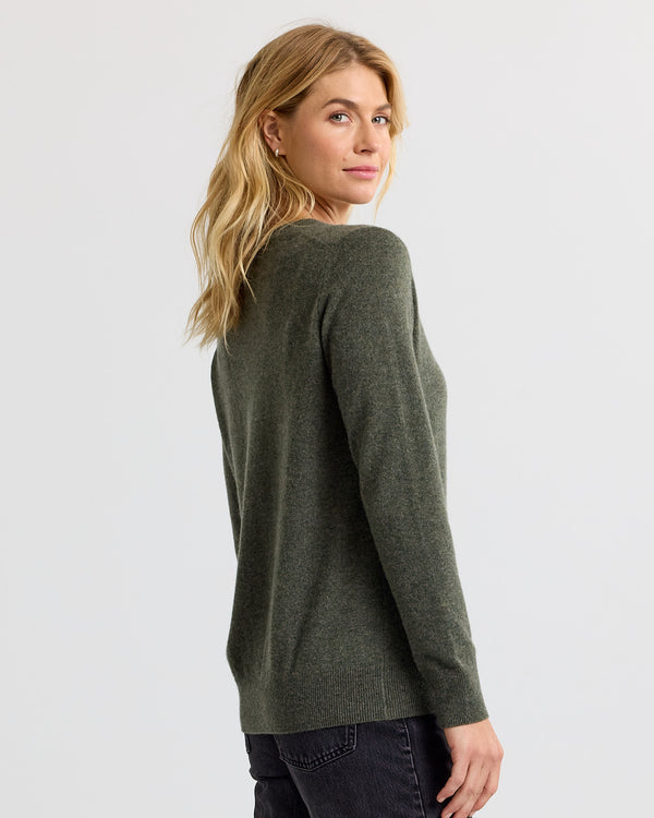 LIFESTYLE / EDITORIAL: Woman wearing dark olive cashmere sweater, looking over shoulder against plain background