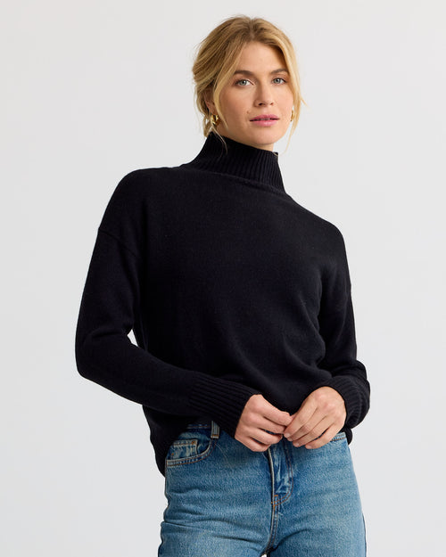 Black cashmere funnel neck sweater with blue jeans against a plain background