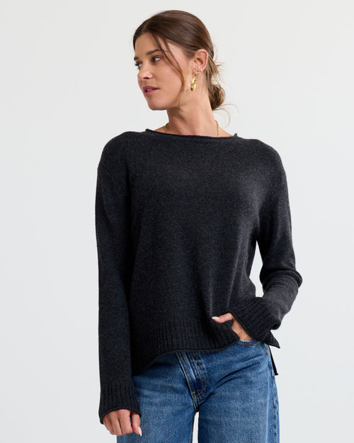 LIFESTYLE / EDITORIAL: Woman wearing charcoal cashmere sweater and blue jeans, looking to the side against a plain background