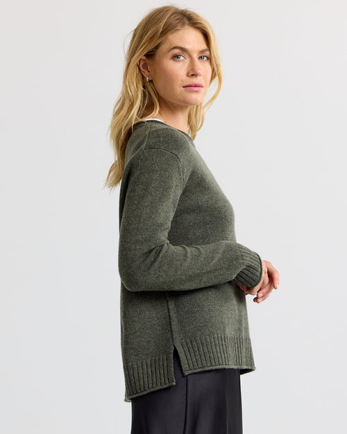 LIFESTYLE / EDITORIAL: Woman in dark olive cashmere sweater, side view, against plain light background