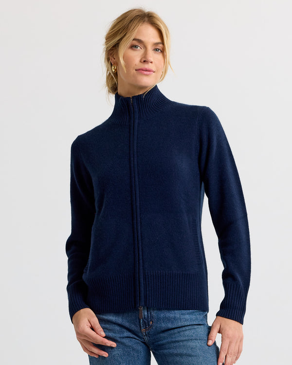 LIFESTYLE / EDITORIAL: Woman wearing navy zip-up cashmere sweater and jeans against plain background