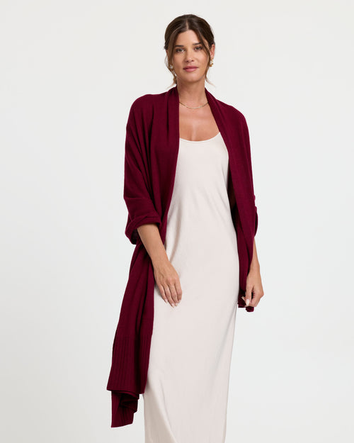 LIFESTYLE / EDITORIAL: Woman wearing a long white dress and a burgundy cashmere shawl standing against a white background
