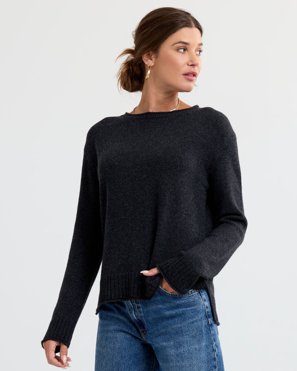 Three-quarter view image of a woman wearing a charcoal cashmere sweater and blue jeans, looking to her left