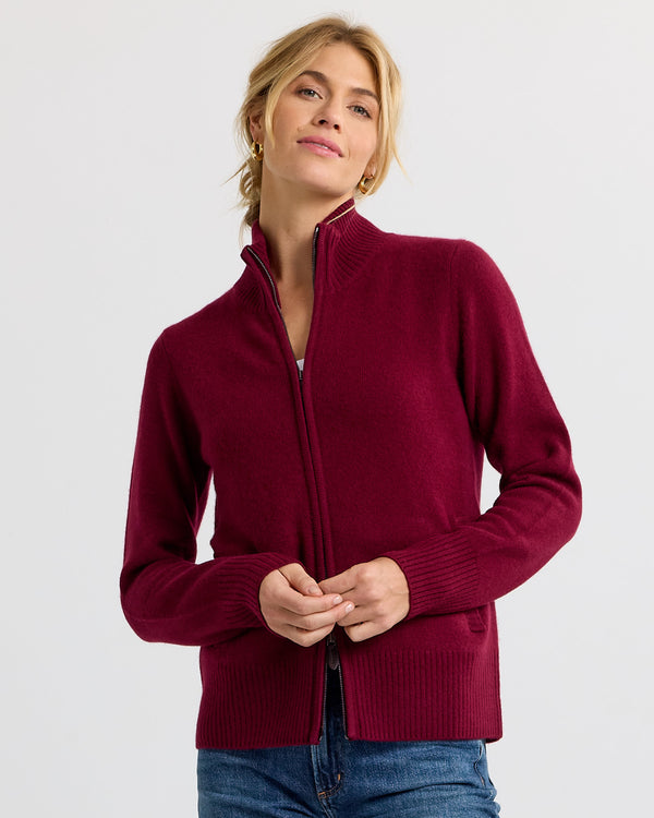 LIFESTYLE / EDITORIAL: Woman wearing a barolo-colored zip-up cashmere sweater with jeans against a plain background
