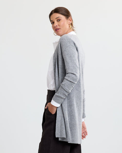 LIFESTYLE / EDITORIAL: Woman wearing long grey cashmere cardigan over white shirt and black pants, side pose against white
